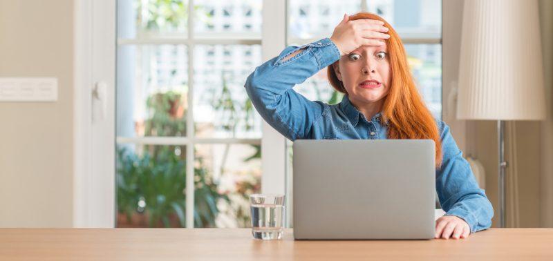 Redhead Woman Using Computer Laptop At Home Stressed With Hand On Head, Shocked With Shame And Surprise Face, Angry And Frustrated. Fear And Upset For Mistake.